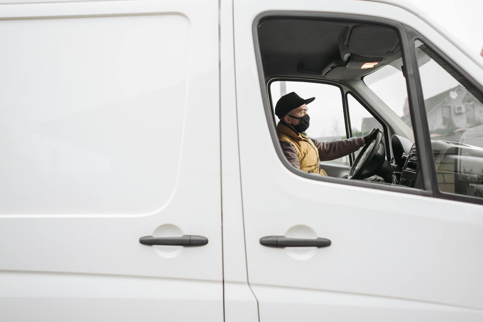 A delivery driver wearing a face mask operates a van, embodying modern safety measures.